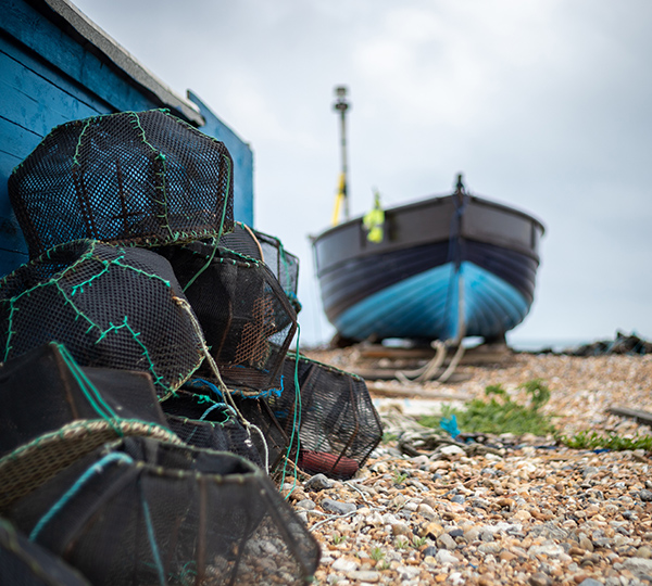 Lobster pots sacked on a pebble beach with a boat in the background